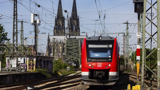 Ein Zug der deutschen Bahn fährt auf die Kamera zu, im Hintergrund sieht man den Kölner Dom.