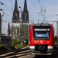 Ein Zug der deutschen Bahn fährt auf die Kamera zu, im Hintergrund sieht man den Kölner Dom.