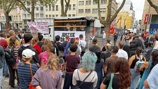 Menschen stehen vor einer Bühne an der ein Banner mit "Justice for Pedro Corona" hängt.