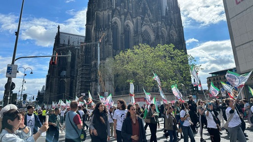 Eine protestierende Menschenmenge mit rot-weiß-grünen Fahnen läuft vor dem Kölner Dom die Straße entlang.