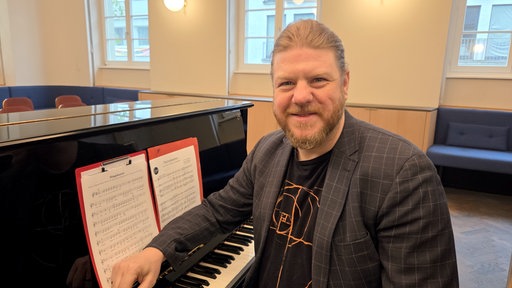 Stimmbildner Keno Brandt sitzt an einem Klavier in einem hell beleuchteten Raum