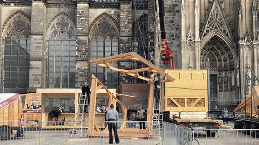 Vor dem Kölner Dom steht ein Holzgerüst, an dem Bauarbeiter arbeiten