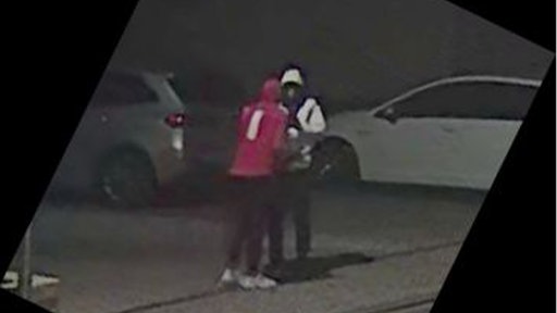 2 Männer in Kapuzenpullovern stehen nachts auf einem Parkplatz, sie stehen nah bei einander