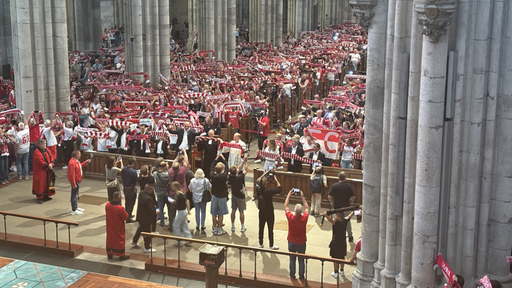 Fans des 1. FC Köln stehen im Kölner Dom und halten ihre rot-weißen Schals in die Luft.