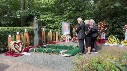 Die Grabstelle von Fritz Schramma umringt von Blumen, davor stehen drei trauernde Menschen in schwarzer Kleidung