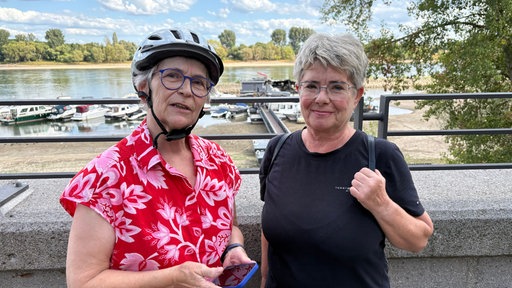 Doris Kallmeyer (links) und Adelheid Hartwig stehen am Rheinufer mit Blick auf das abgebrannte Boot.