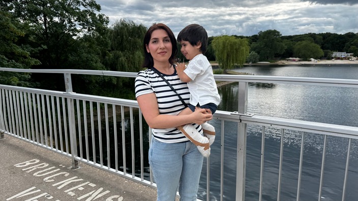 Fahime Ghahestani hält ihren Sohn Raybod auf dem Arm und steht auf einer Brücke am Fühlinger See.