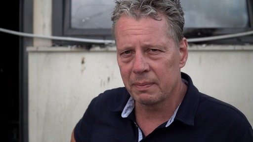 Jörg Blöck, Pächter des Sürther Bootshaus, steht vor dem abgebrannten Boot.