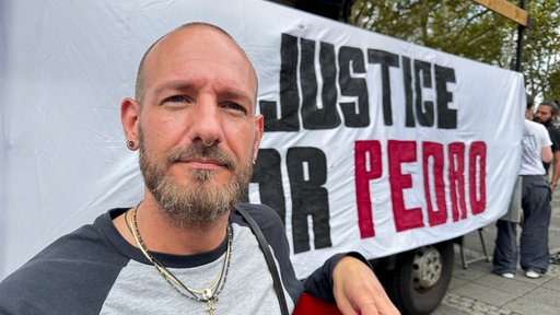 Julian steht vor einem Banner auf dem Justice for Pedro steht.