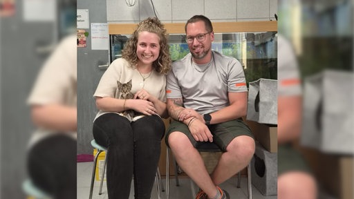 Kätzchen Olivia sitzt auf dem Schoß einer Frau, daneben sitzt ein Mann.