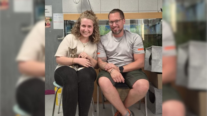 Kätzchen Olivia sitzt auf dem Schoß einer Frau, daneben sitzt ein Mann.