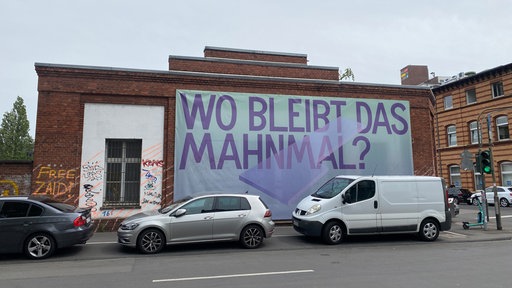 Protestbanner mit der Aufschrift "Wo bleibt das Mahnmal" hängt an einer Hauswand