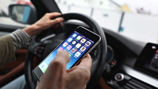 Ein Autofahrer hält während der Fahrt ein Smartphone in der Hand