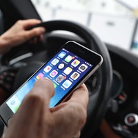 Ein Autofahrer hält während der Fahrt ein Smartphone in der Hand