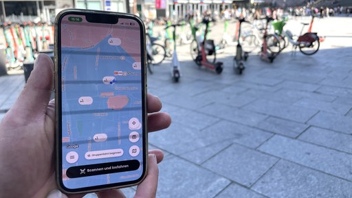 Eine Person nutzt eine App, um den Standort eines E-Scooters im öffentlichen Raum zu kontrollieren.