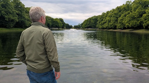 Markus Weber steht mit dem Rücken zur Kamera vor dem Weiher im Kölner Blücherpark.