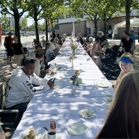 mehrere menschen sitzen an einer langen, gedeckten Tafel und unterhalten sich