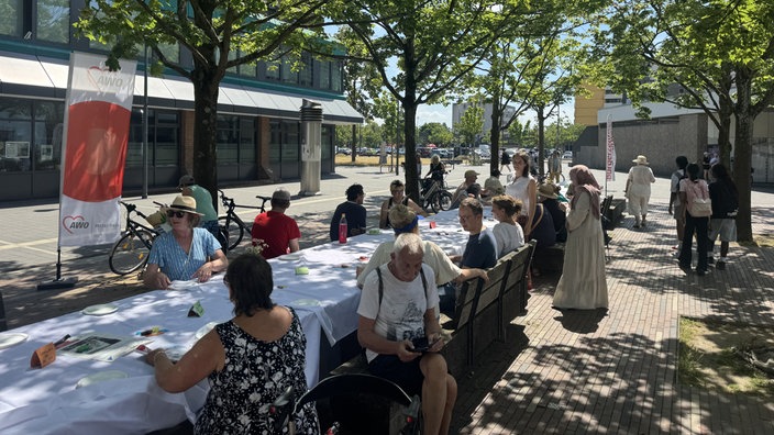 mehrere menschen sitzen an einer langen, gedeckten Tafel und unterhalten sich