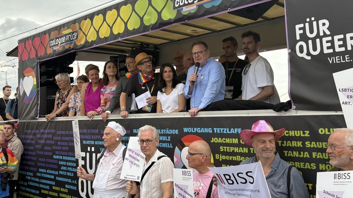 Köln Oberbürgermeister Torsten Burmester steht mit weiteren Personen und einem Mikrofon in der Hand auf einem Festwagen.