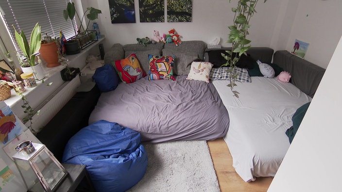 Ausschnitt der Wohnung des Erziehers. Eine Couch mit bunten Kissen. Links im Bild sieht man einen blauen Sitzsack und eine Fensterbank mit Pflanzen.