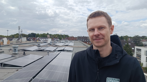 Mathias Weidle von Green Plant Energy steht auf einem Flachdach auf dem viele Solarpanele angebracht wurden. 