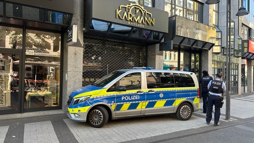 Die Polizei steht mit einem Einsatzfahrzeug und zwei Beamten vor dem Tatort, dem Uhrengeschäft in der Kölner Innenstadt