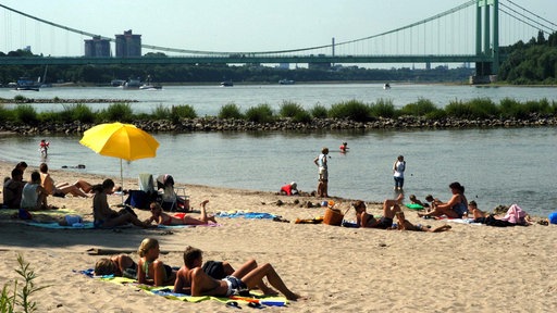 Menschen sitzen am Strand der Rodenkirchener Riviera, im Hintergrund eine Autobahnbrücke.