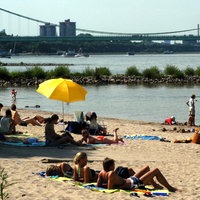 Menschen sitzen am Strand der Rodenkirchener Riviera, im Hintergrund eine Autobahnbrücke.
