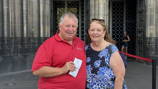 Roslyn und Tony aus Australien stehen mit Ticket vor dem Kölner Dom