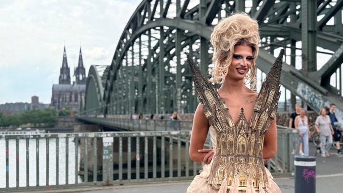 Eine Person trägt ein kleid, das ein Abbild des Kölners Doms ist. In der Ferne sieht man den Dom.