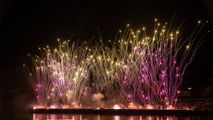 Eine bunte Feuerwerksfontaene die auf dem Rhein steht und nach oben schießt. 