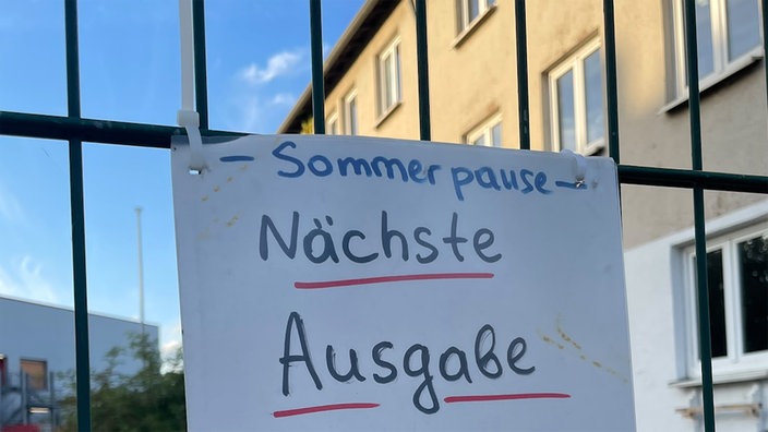 An einem Metallzaun hängt ein weißes Schild mit der Aufschrift: "- Sommerpause - Nächste Ausgabe"