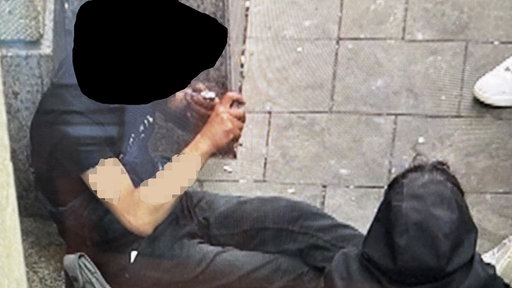 Eine Person sitzt auf dem Bürgersteig und konsumiert Drogen über eine Pfeife