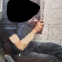 Eine Person sitzt auf dem Bürgersteig und konsumiert Drogen über eine Pfeife