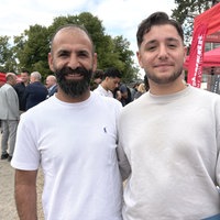Roni Özkul (Sohn) und Gökmen Özkul (Vater) stehen auf einer Ausbildungsmesse neben einem roten Zelt