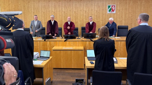 Richter stehen hinter einem Tisch am Oberverwaltungsgericht Münster.