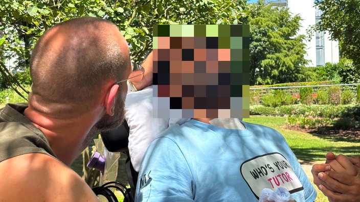 Pedro Corona sitzt im Rollstuhl in einem Park mit seinem Partner Julian an seiner Seite