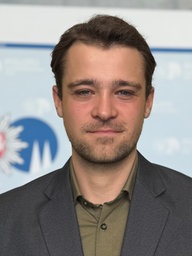 Benno Groß steht vor einer Wand mit Logo der Polizei Köln