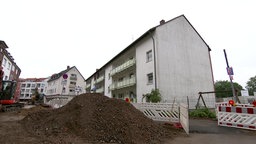 eine Baustelle mit einem aufgeschütteten Erdhaufen. Dahinter ein Mehrfamilienhaus