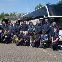 Eine Gruppe von Menschen in blauer THW-Kleidung, in der Mitte ein Hund, dahinter ein THW-Bus.