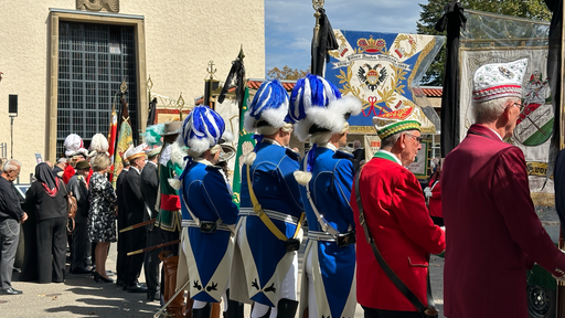 Mehrere Personen stehen in traditioneller Karnevals-Uniform vor einer Kirche.