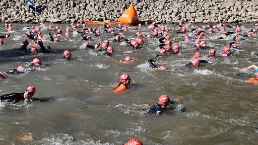 Menschen mit roten Badekappen schwimmen im Rhein