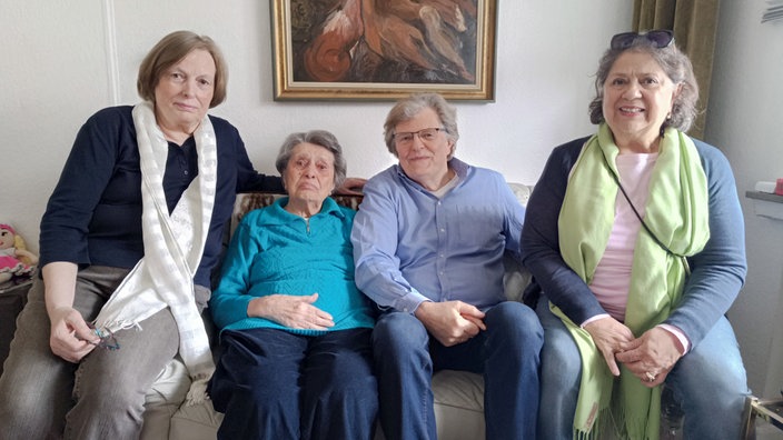 Die Tochter der Mieterin, die Mieterin selbst, der Sohn und die Schwiegertochter sitzen auf dem Sofa.