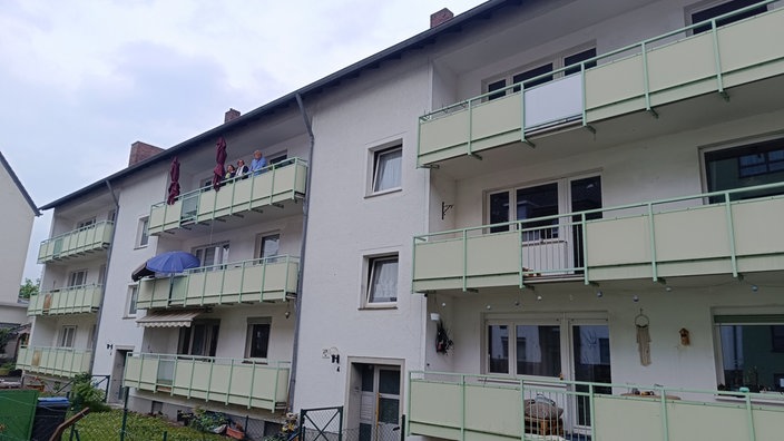 Fassade eines Mehrfamilienhauses. Auf dem Balkon oben links stehen drei Frauen.