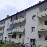 Fassade eines Mehrfamilienhauses. Auf dem Balkon oben links stehen drei Frauen.