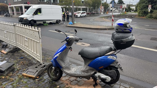 Ein Roller steht an einer Straßenkreuzung, im Hintergrund ist die Unfallstelle zu erkennen.