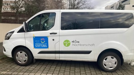 Ein weißer Bus mit dem Aufdruck "Aktion Nachbarschaft" und dem Aufdruck "Fernsehlotterie Stiftung" auf einem Parkplatz