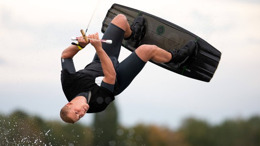Mann auf Wakeboard hält sich an Seil fest und schlägt ein Salto
