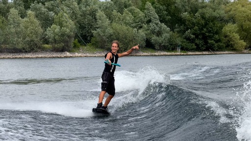 Mann der auf einem Wakebaord steht und dabei ein Schnur hält.