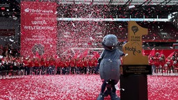 Konfetti fliegt durch die Luft im Rhein-Energie-Stadion. Im Vordergrund ein Preis mit der Aufschrift 17 000 Kinder und ein Maskottchen daneben. Im Hintergrund viele Kinder.